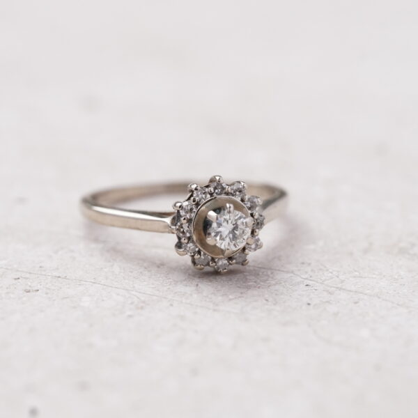 Anillo tipo flor con diamante central 0.20CT y bisel de diamantes en oro blanco